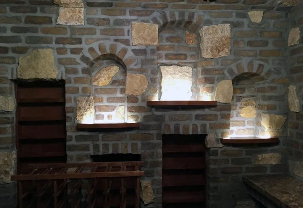 Rustic stone wall with illuminated shelves and a wine rack in a cozy cellar setting.