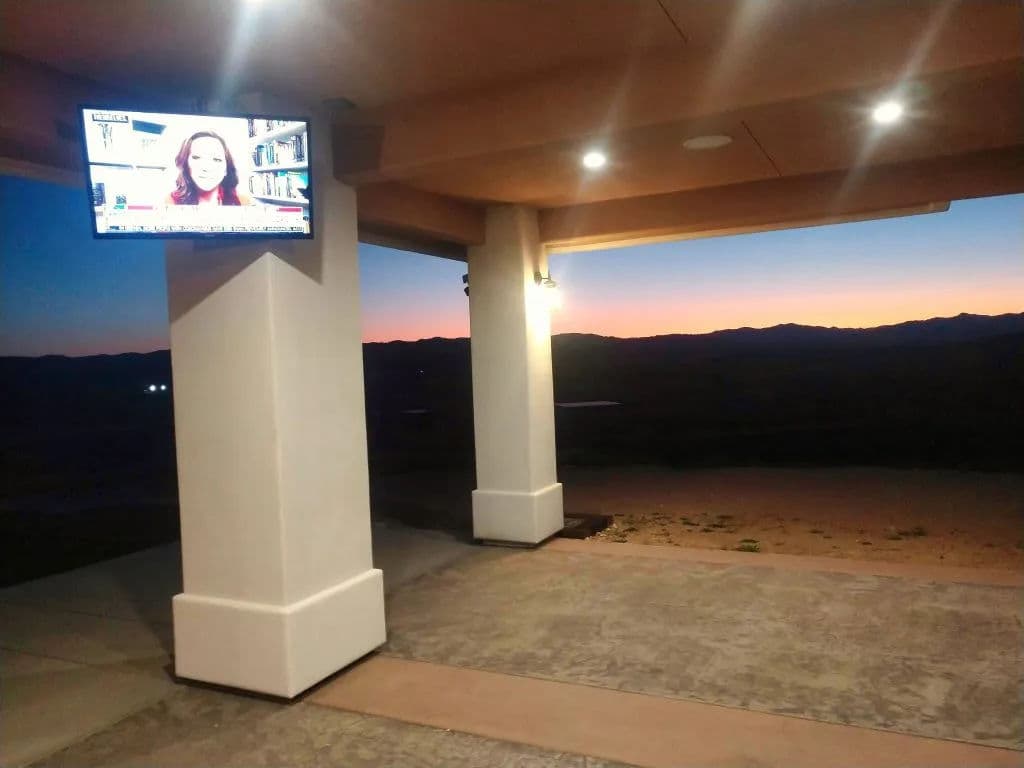 Patio view at sunset with a TV showing news, surrounded by mountains and lit ambiance.