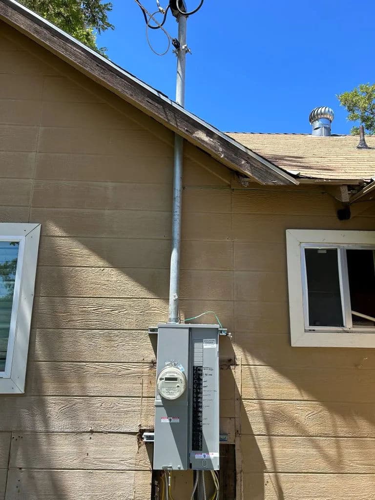 Electrical service panel mounted on exterior wall of a house with clear blue sky background.