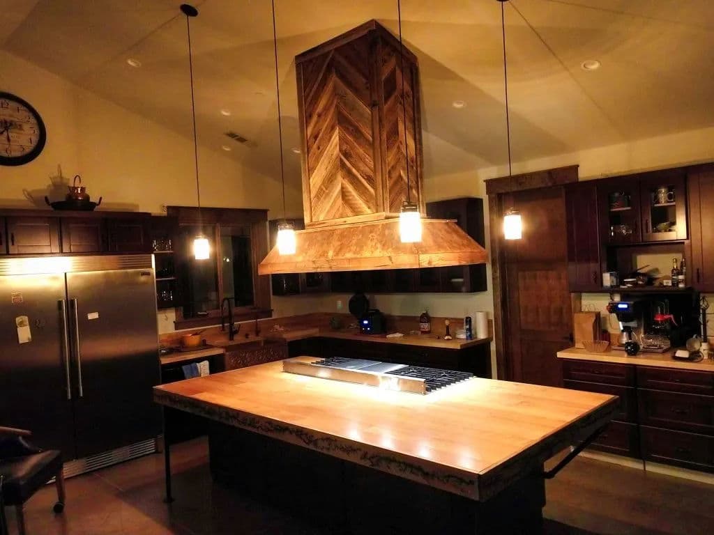 Modern kitchen with a large wood island, decorative range hood, and stylish pendant lighting.