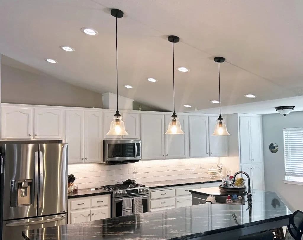 Modern kitchen with white cabinetry, stainless steel appliances, and pendant lights over a granite island.