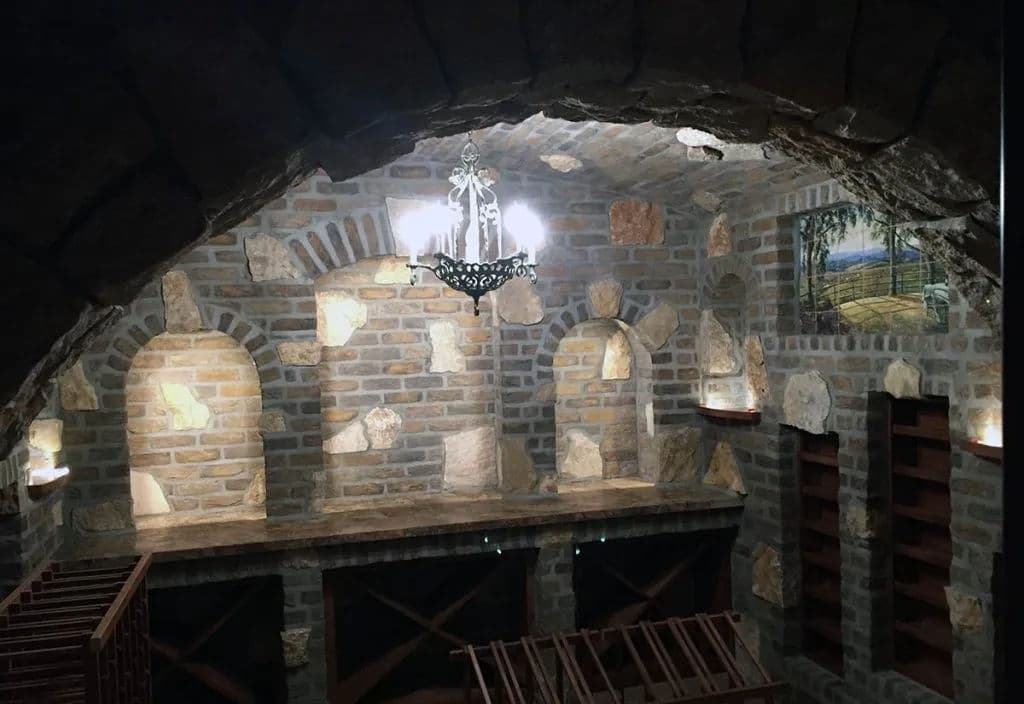 Elegant stone wine cellar with chandelier, shelves, and warm ambient lighting.