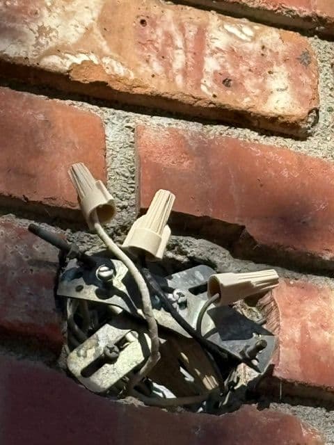 Electrical junction box with wire connectors against a brick wall.