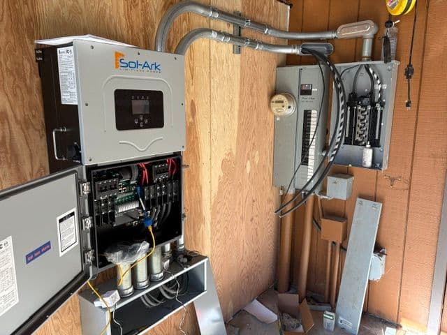 Sol-Ark solar inverter and electrical panel installation in a wooden utility space.