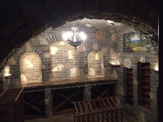 Wine cellar with stone walls, wooden racks, and elegant chandelier for ambiance.