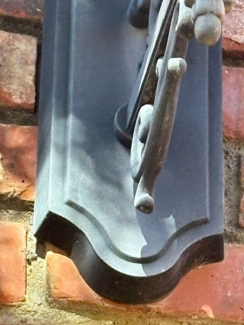 Close-up of a decorative black metal door knocker on a brick wall.
