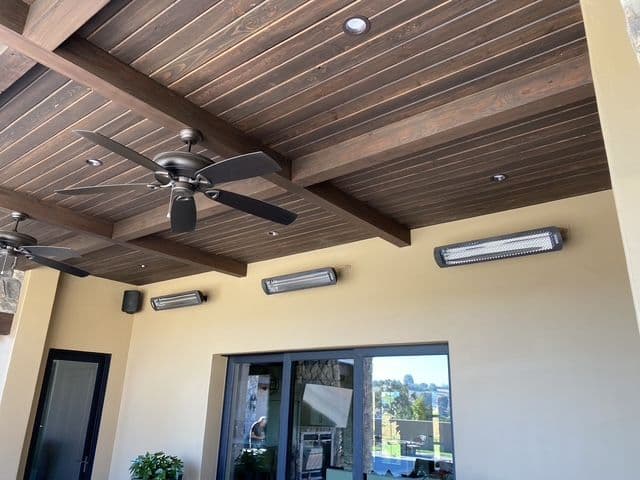 Modern outdoor ceiling with wooden beams, fans, and heating lights in a stylish patio setting.