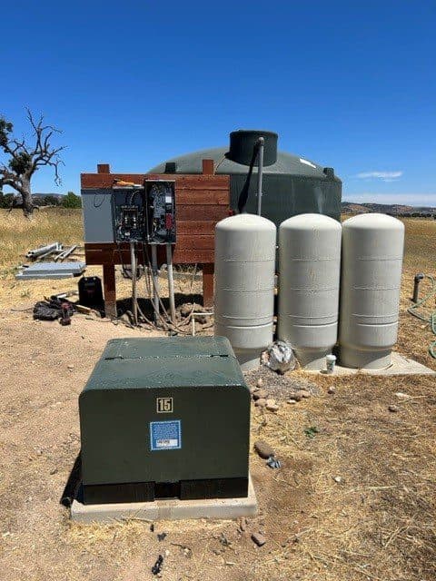 Water storage system with green tanks and control panel in rural landscape.