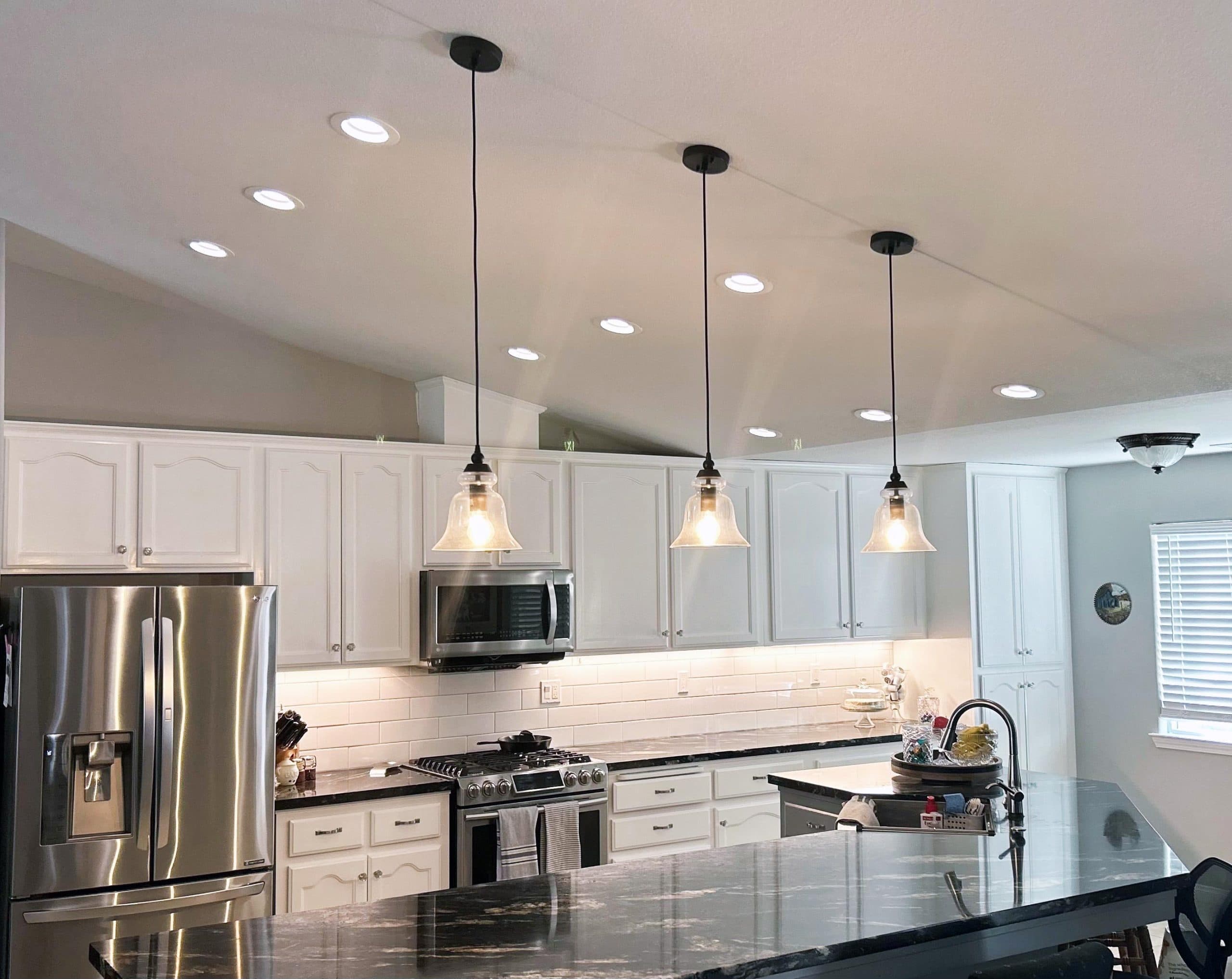 Modern kitchen with pendant lights over an island, white cabinets, and stainless steel appliances.
