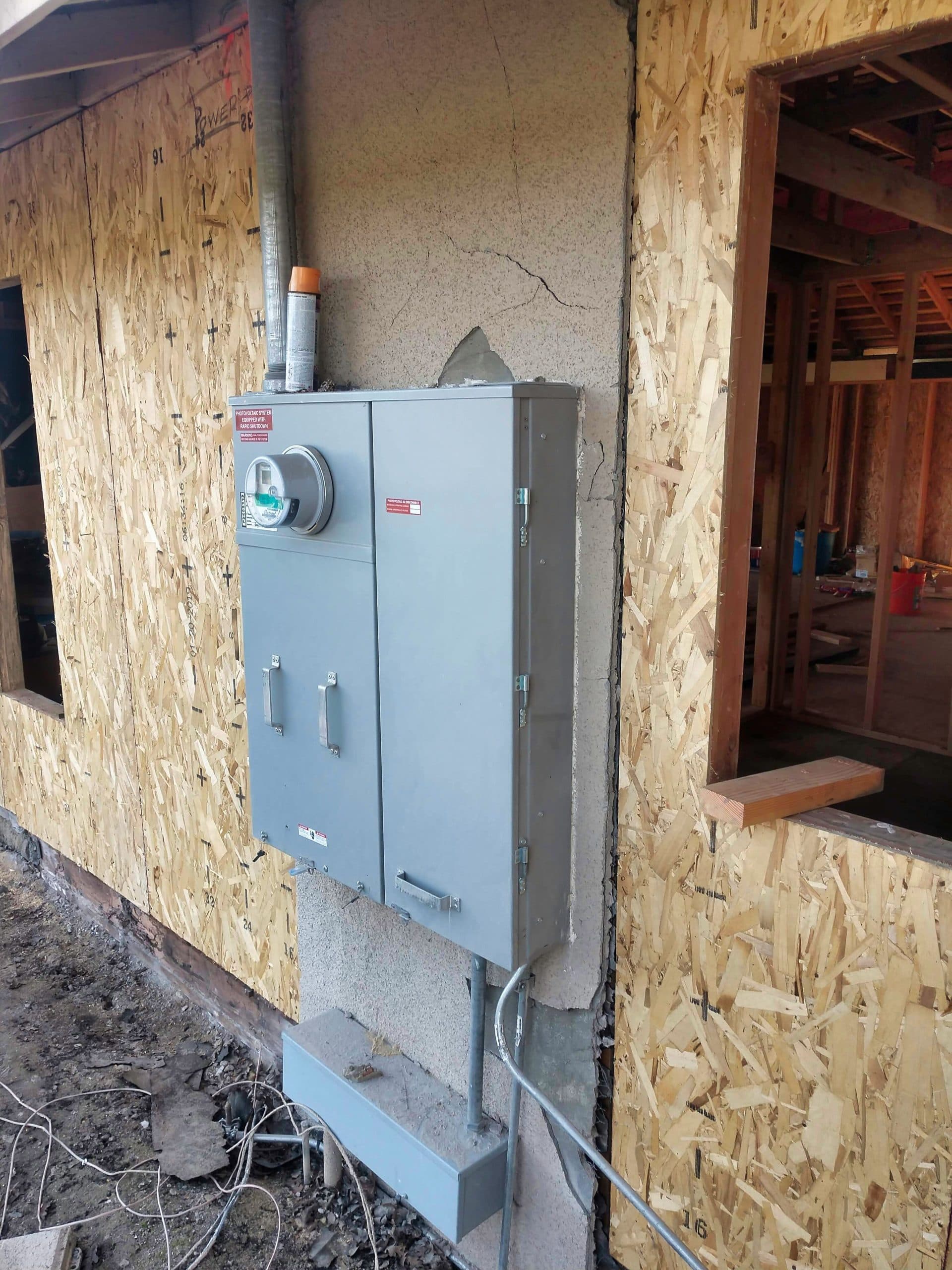 Electric meter box installed on a new home's exterior wall, surrounded by construction materials.