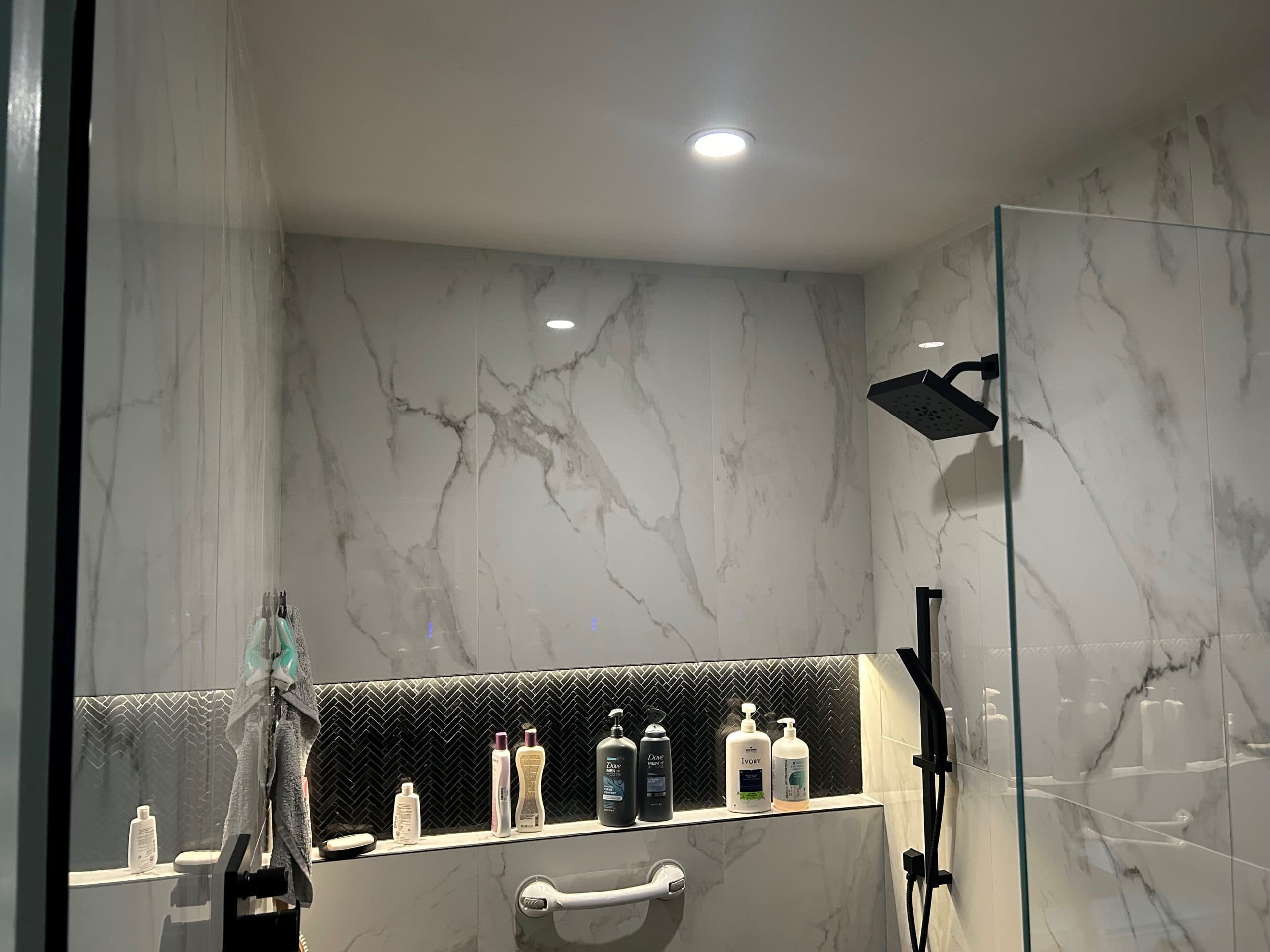 Modern bathroom with marble walls, glass shower, and organized toiletries on shelves.